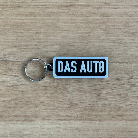 a picture of the Das Auto keychain with white lettering and boarder on black background