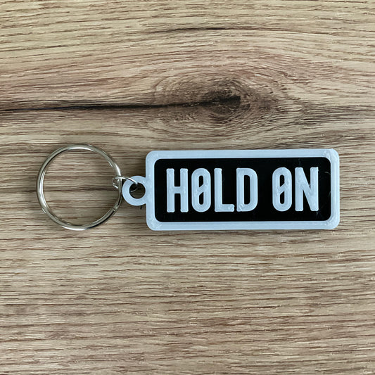 An image of the Hold on keychain in the colour black with with lettering and borders.