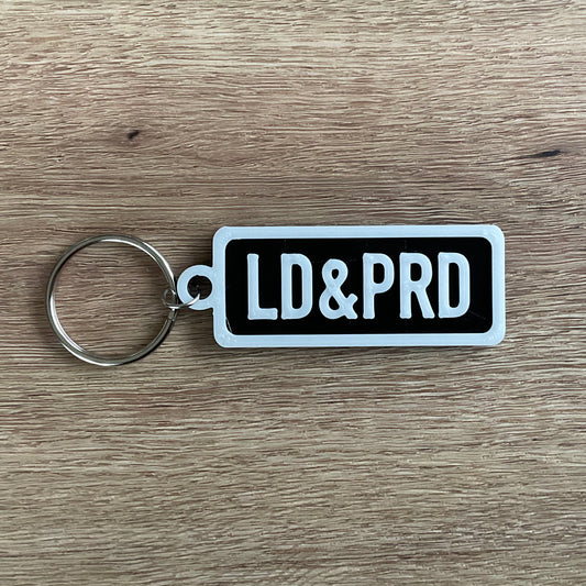 an picture of the white on black version of the loud and proud keychain. 