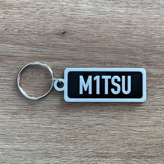 An image of the numberplate Mitsubishi keychain with white lettering and black background.