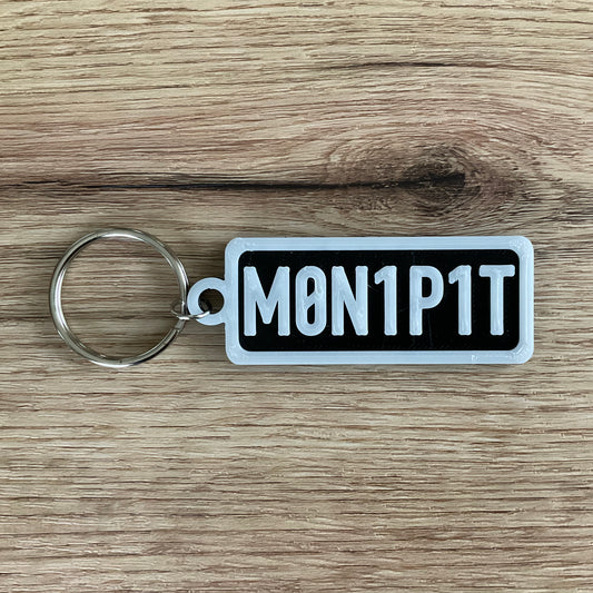 An image of the Money pit keychain in the colour black with white lettering and border.