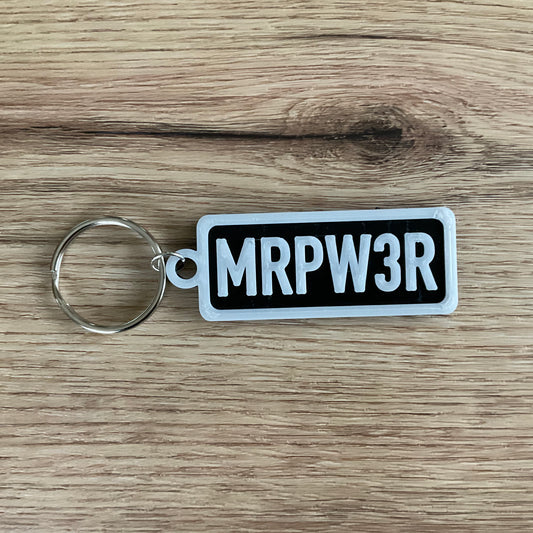 An image of the keychain MRPWER keychain in the colour black with white lettering and border.