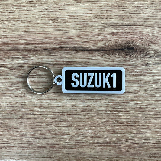 An image of the black Susuki keychain with white lettering and border 