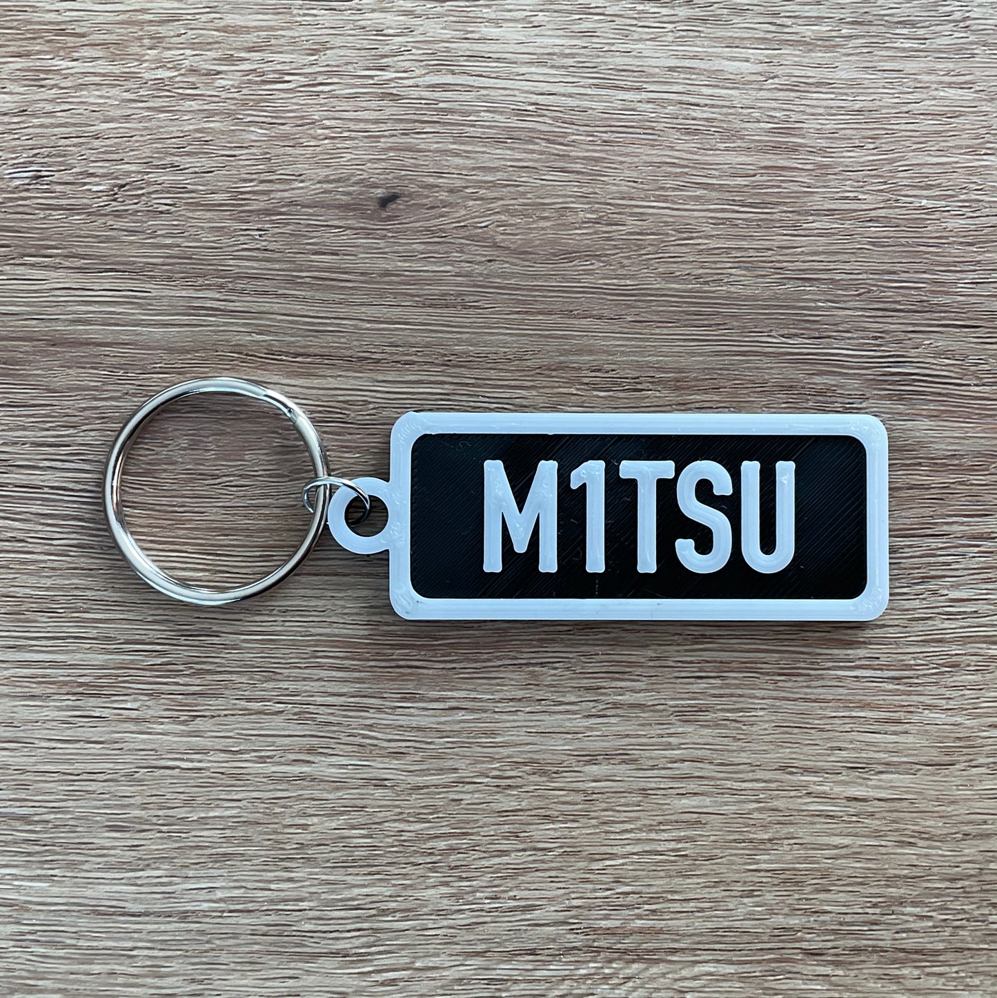 An image of the numberplate Mitsubishi keychain with white lettering and black background.