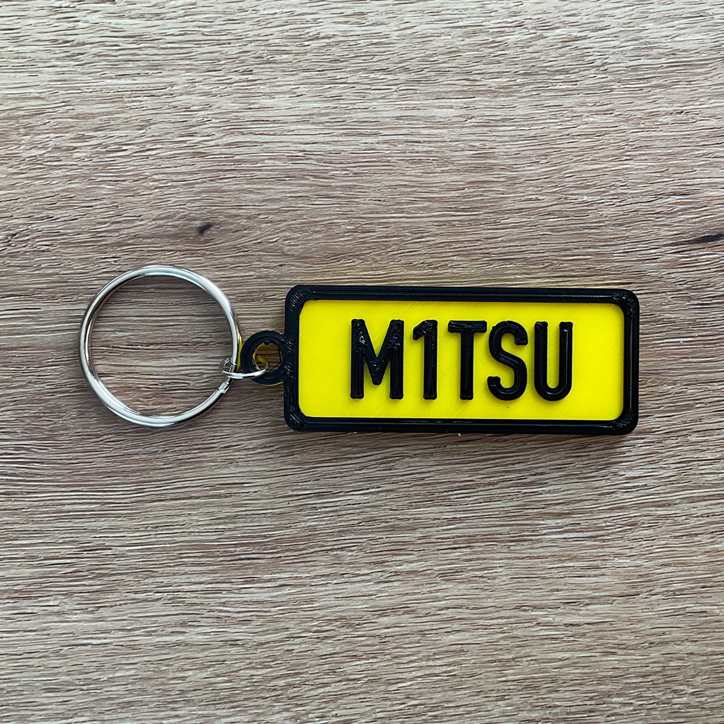 An image of the Yellow Mitsubishi numberplate keychain with black border and lettering.