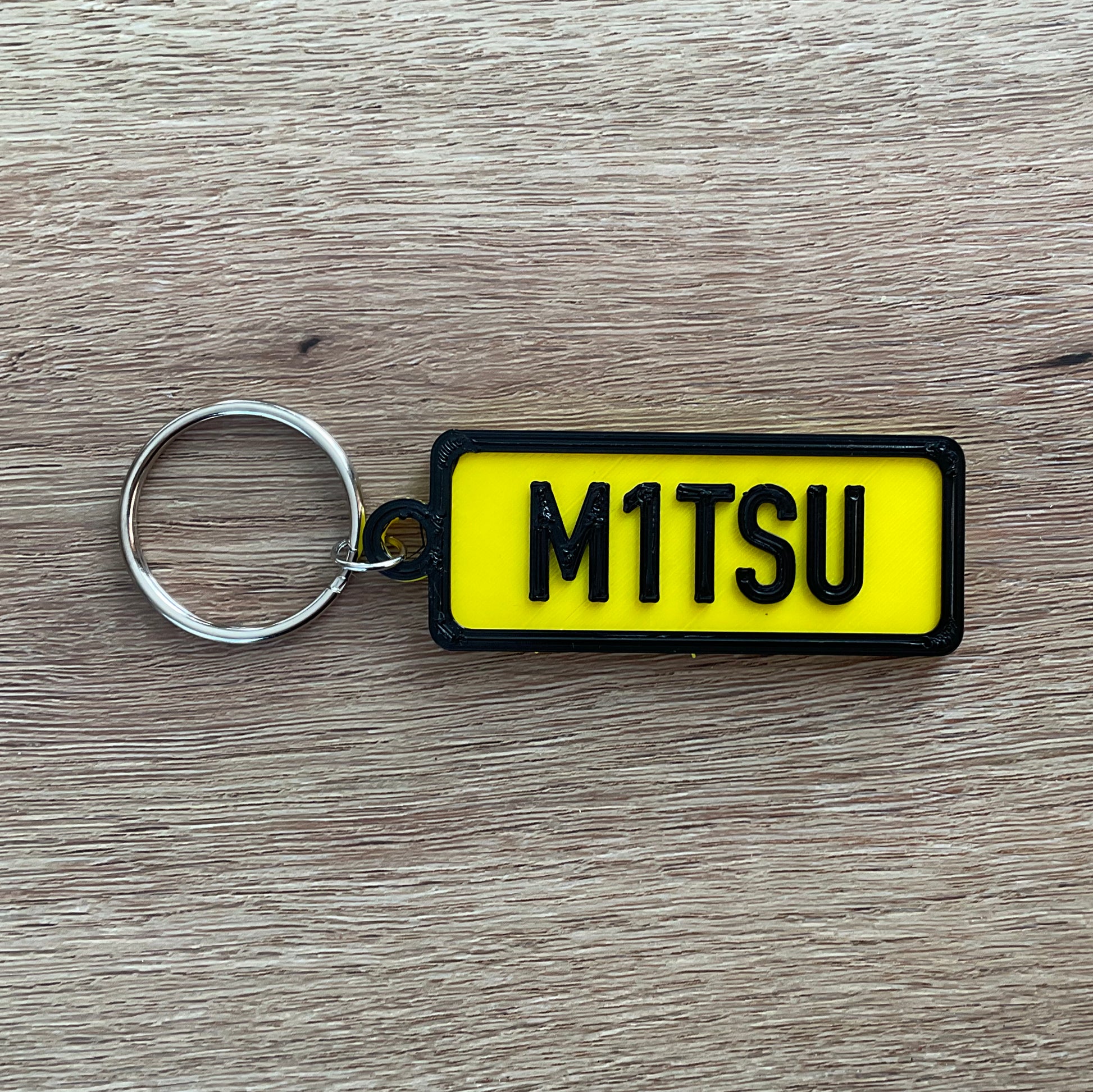 An image of the Yellow Mitsubishi numberplate keychain with black border and lettering.